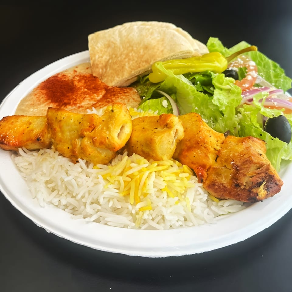 Chicken kabob with rice, hummus, pita bread, and a fresh salad on a white plate.