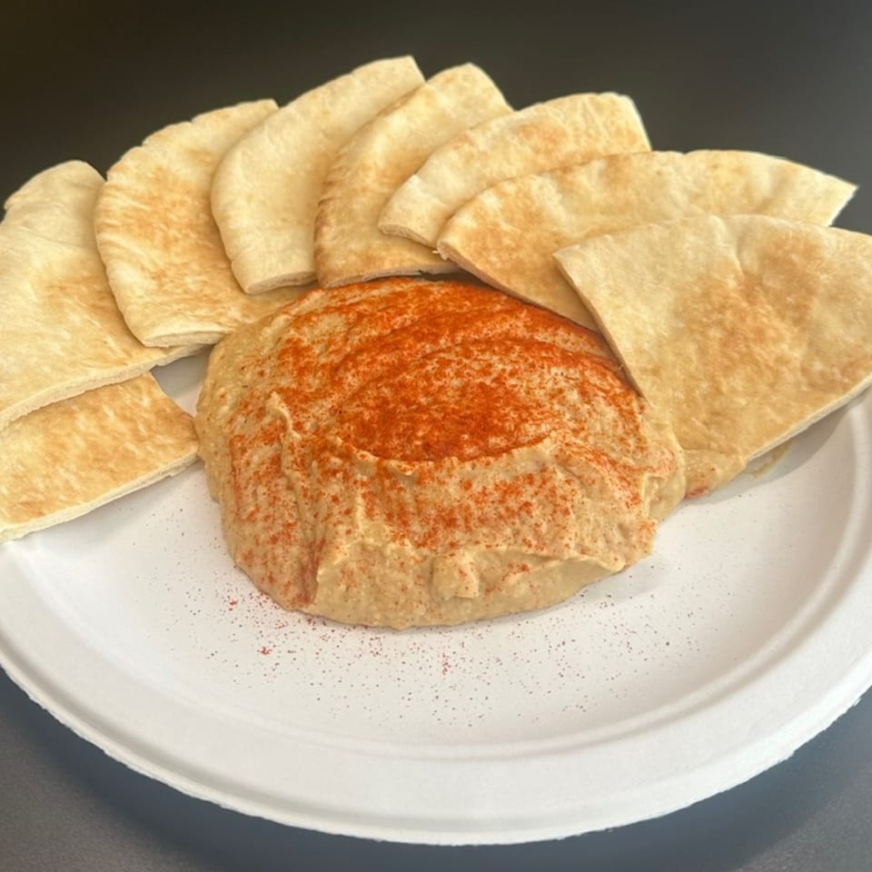 Creamy hummus topped with paprika, surrounded by warm pita bread triangles on a white plate.