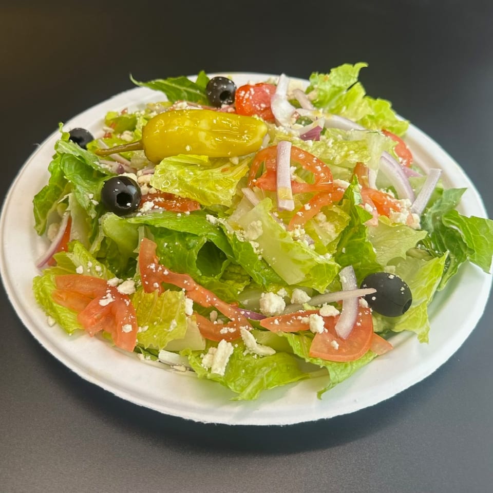 A fresh Mediterranean salad with lettuce, tomatoes, onions, olives, feta cheese, and a pepperoncini.
