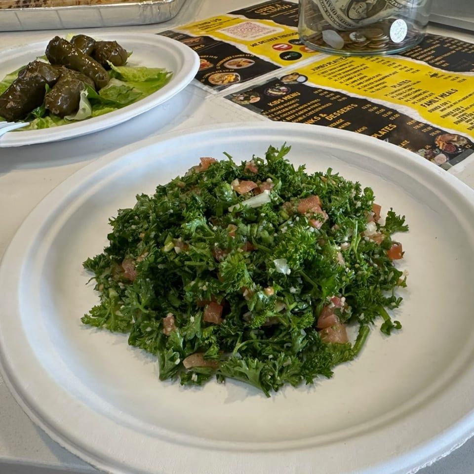 A vibrant tabbouleh salad with parsley and tomatoes on a white plate, next to stuffed grape leaves.